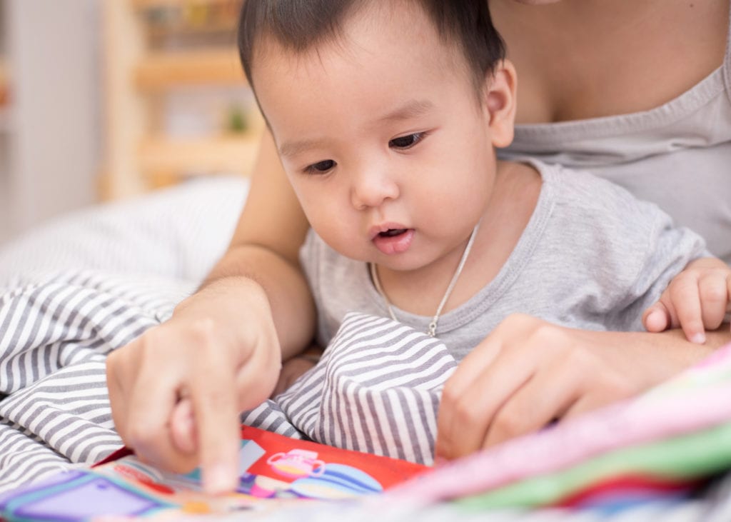 baby reading book with caregiver